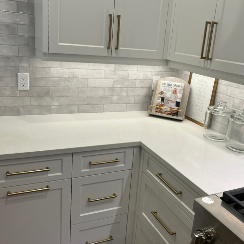 A modern kitchen counter with light grey cabinets, a white subway tile backsplash, and three glass jars for storage.